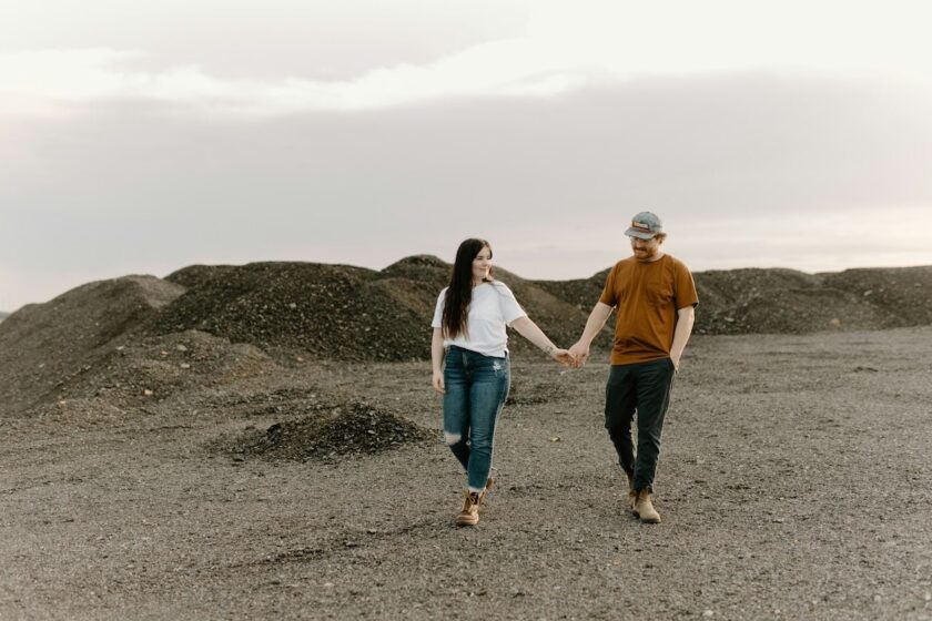 Un uomo e una donna camminano mano nella mano in un campo aperto, simbolo di libertà e intimità durante un viaggio di coppia romantico.