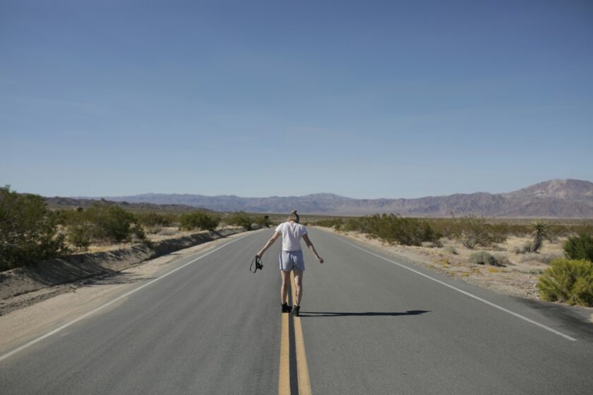 Viaggiatore con zaino che fa autostop su una strada aperta