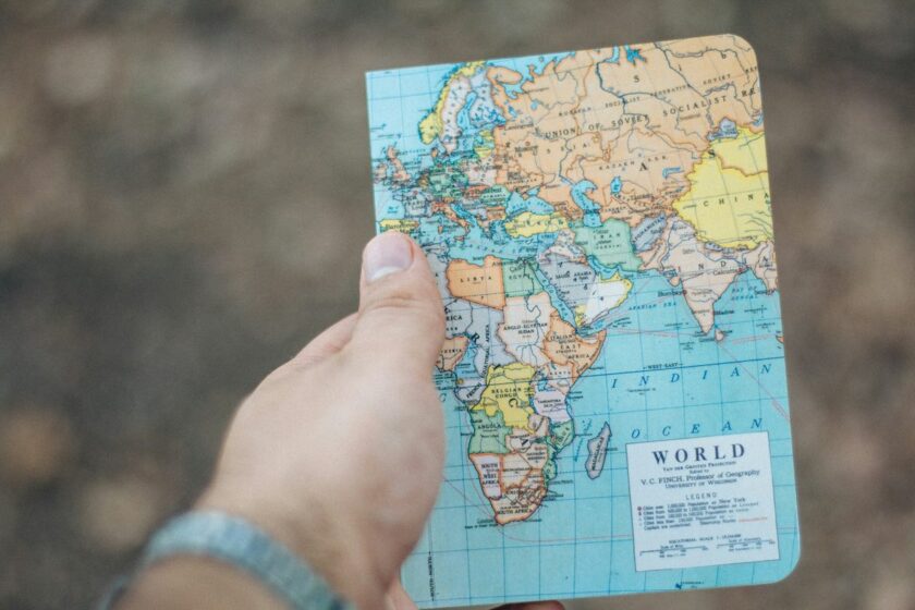 Persona con zaino davanti a una grande mappa del mondo che indica possibili rotte di viaggio