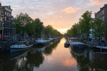Vista dei canali di Amsterdam al tramonto con case colorate e biciclette, simbolo di sicurezza e serenità urbana.