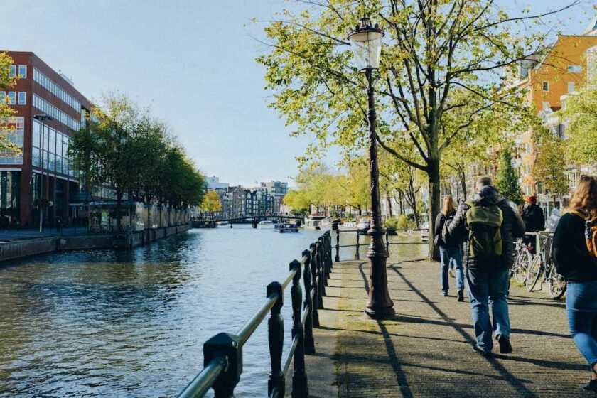 Turisti che passeggiano lungo un canale di Amsterdam in pieno giorno, esempio della sicurezza e vivibilità della città.