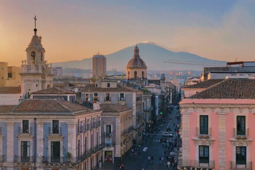 Vista del centro storico di Catania con palazzi barocchi e l’Etna innevata sullo sfondo