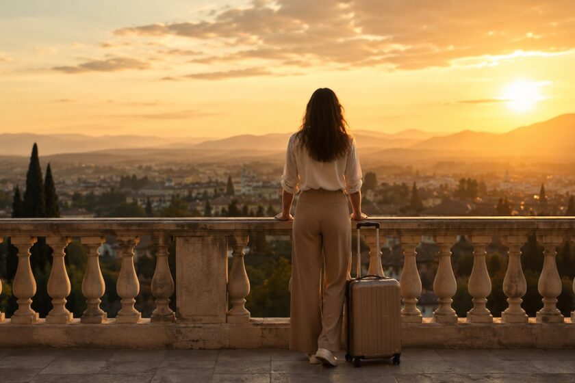 Donna che osserva un paesaggio al tramonto con valigia, immagine evocativa per frasi e citazioni di viaggio.